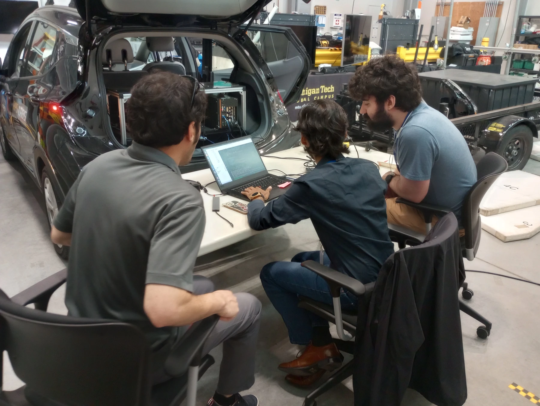 Retrospect team working together beside a Michigan Tech research vehicle at ACM